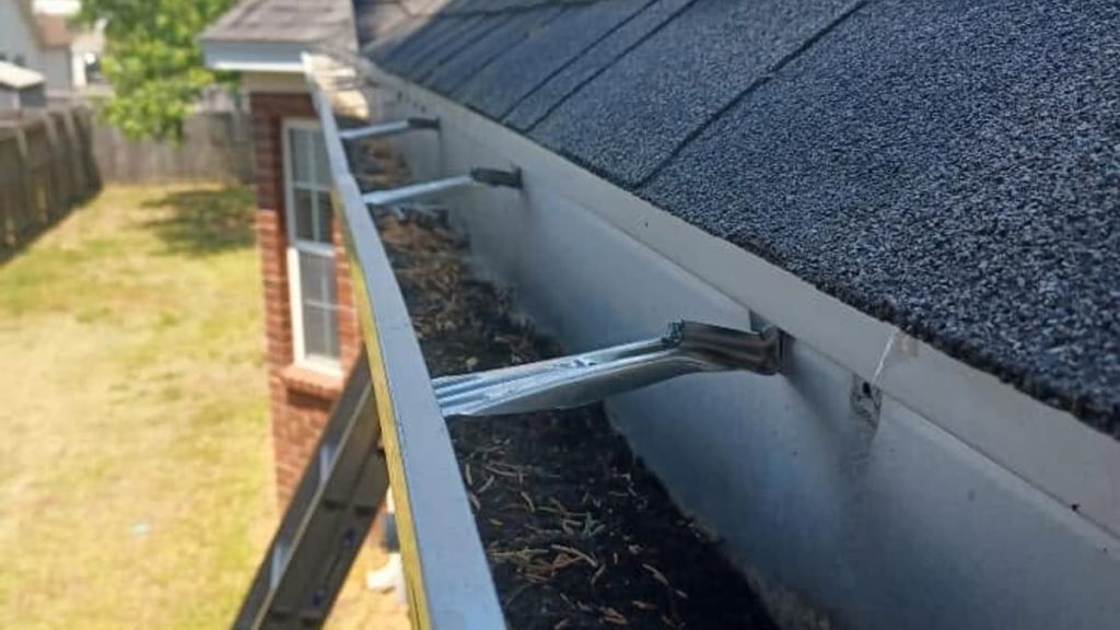 A rain gutter packed with leaves and debris, pulling away from the fascia board