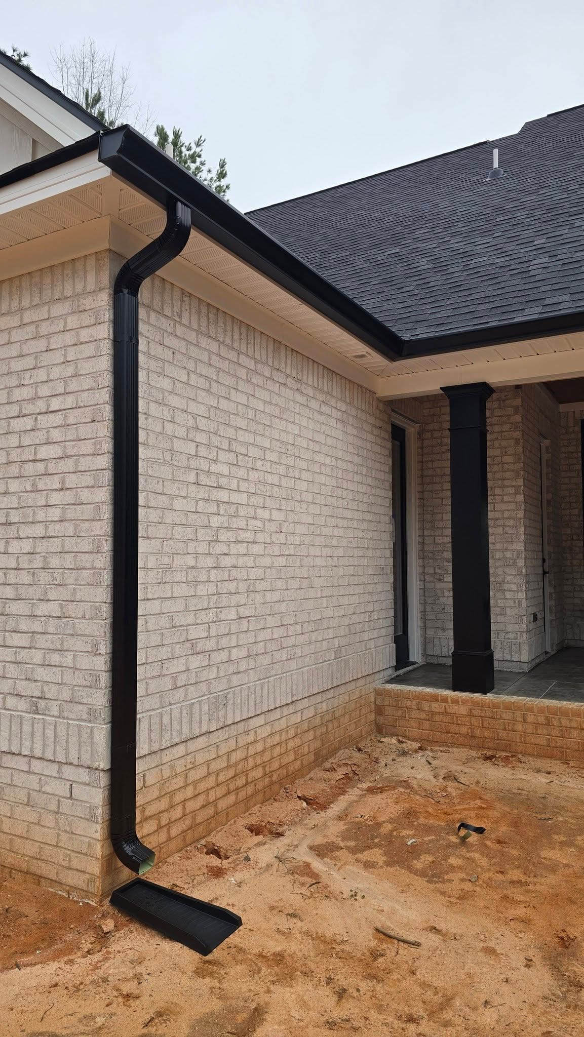 Black downspout and splash block carrying water away from a white brick home