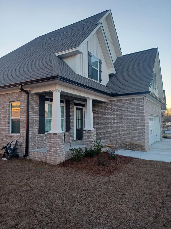 Brick and board-and-batten home with dark gutters photographed at dusk