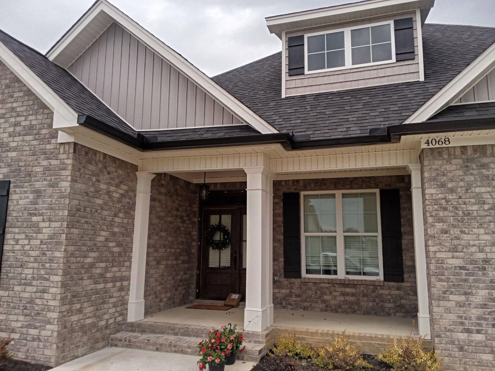 Brick craftsman home with dark seamless gutters along the front porch roofline