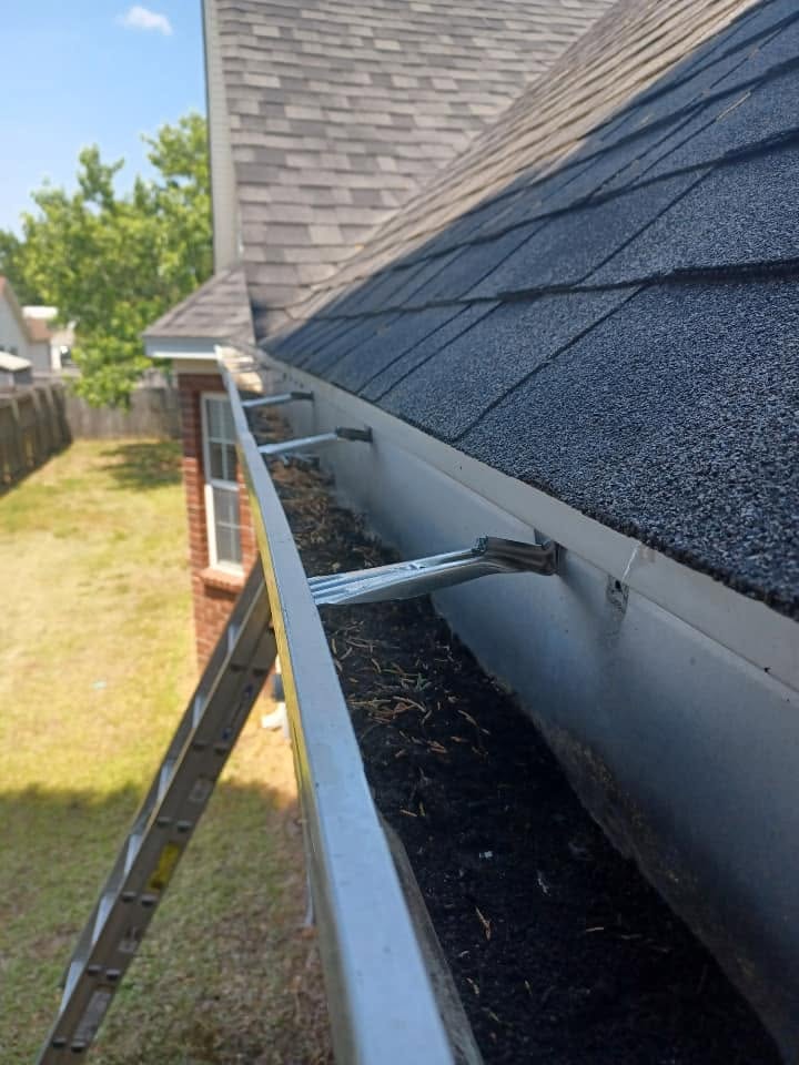 Clogged gutter packed with debris and a loose hanger before repair
