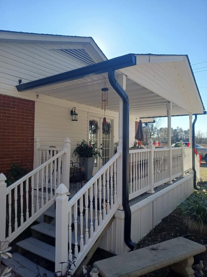 Covered porch with dark seamless gutter and downspout on a white farmhouse