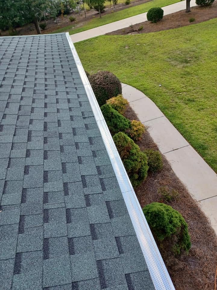Gutter guard running the length of a shingle roofline above landscaped beds