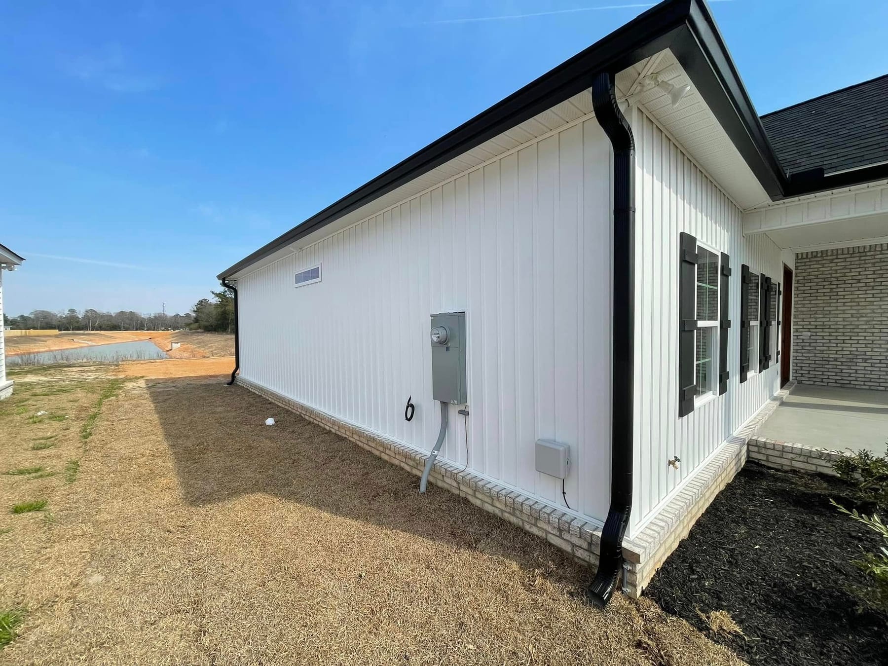 White board-and-batten home with black seamless gutters and a corner downspout